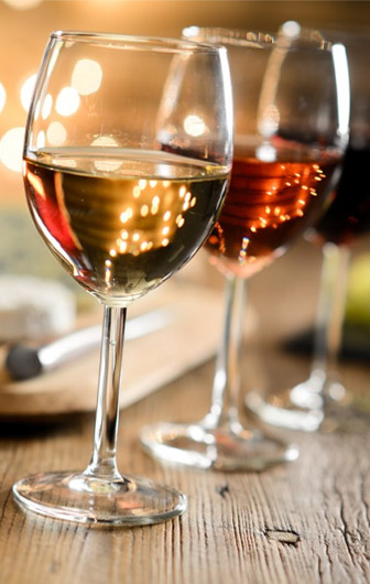 trois verres à pieds remplis de vin blanc (premier plan), vin rosé (second plan) et de vin rouge (arrière plan)